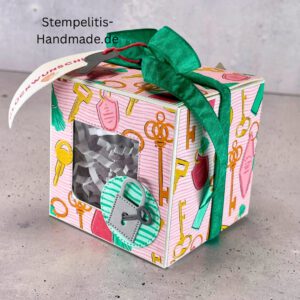 handdekorierte Fensterschachtel mit Glückwunsch-Anhänger, Geschenkbox mit Schlüsselmotiv und grünem Band, Nahaufnahme Fenster der Schachtel mit Füllung, runder Anhänger mit Schloss und Schlüssel, Schachtel geöffnet mit sichtbarem Inhalt, Glückwunsch-Tag an Geschenkbox, Geschenkverpackung für Einzug oder Prüfung